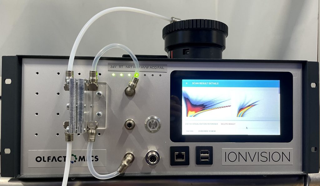 IonVision in the membrane measurement setup. An aluminum block with the membrane is attached to the front of the device. A headspace chamber is placed on top of the device, with a sampling tube coming from it to the membrane block.
